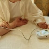 Tensiometru automat pe o masă, lângă un pahar cu apă, folosit pentru măsurarea tensiunii acasă